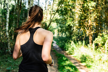 Young fitness woman in black sportwears running at morning forest trail. Rear view.