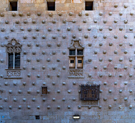 Facade of La Casa de las Conchas with wrought iron windows, moldings with religious motifs in bas-relief and rock shells in Salamanca in Spain.