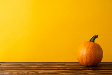 Rustic harvest arrangement featuring pumpkin on a wooden table against an autumn-themed orange backdrop with empty space for text