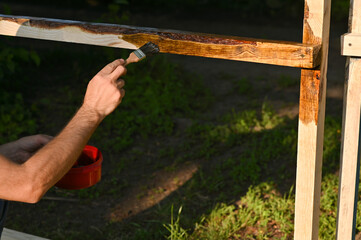 A man paints wood. A person paints a wooden bar with a brush