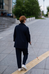 Blind businesswoman walking along tactile tiles with a cane. 