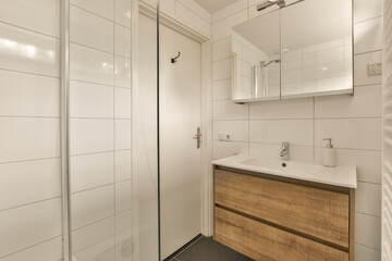 a bathroom with white tiles on the walls and wood cabinetd vanity in the corner, next to a glass shower door