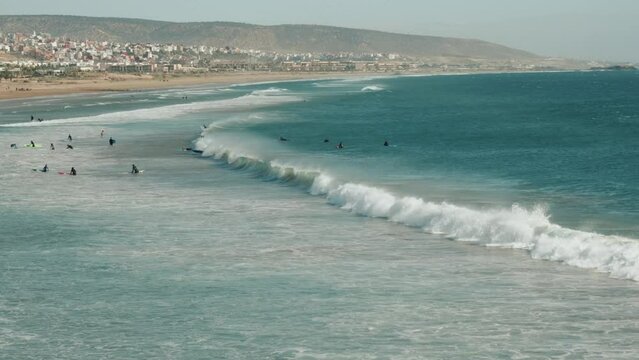 Wide view of a beach, shore and people surfing on sea waves in Agadir, Morocco.
