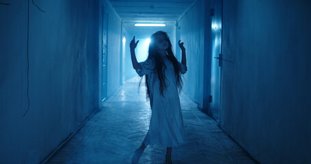 Little girl in white dress looking like a ghost carelessly running down the hallway of a haunted...