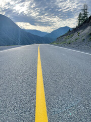 Asphalt road with yellow line in the mountains under cloudy sky.