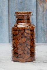 Fresh almond nuts into a glass jar with a closed lid isolated on a marble background. Front view.
