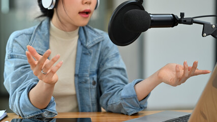 Smiling young woman radio host in headphone talking through microphone for recording conversation...