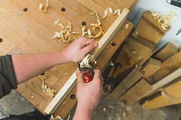 Closeup carpenter shaving a wooden board with a hand planer, wooden chips on the table. High...