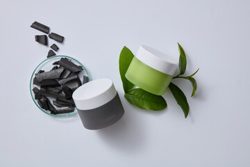 Bamboo charcoal and green tea leaves are decorated on a light gray background with unbranded cosmetic bottles. Scene for advertising and branding for cosmetics with natural ingredient