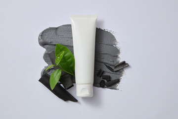 A white cosmetic tube unbranded displayed on mask texture with bamboo charcoal and tea leaves. Bamboo charcoal and green tea are two effective cleansing ingredients in facial cleansers for men