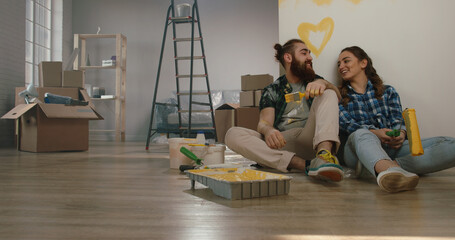 Newlywed caucasian couple are relaxing during renovation of their new home,sitting on the floor positively smiling - new life, mortgage concept 
