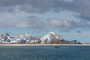 pond with little waves and snowy rocky mountains with dense clouds