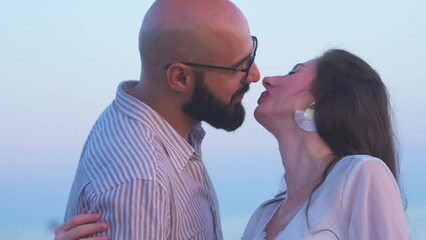 Medium close up shot of pregnant couple at the beach, touching the mother's belly and then tilting the camera up to show them kissing each other