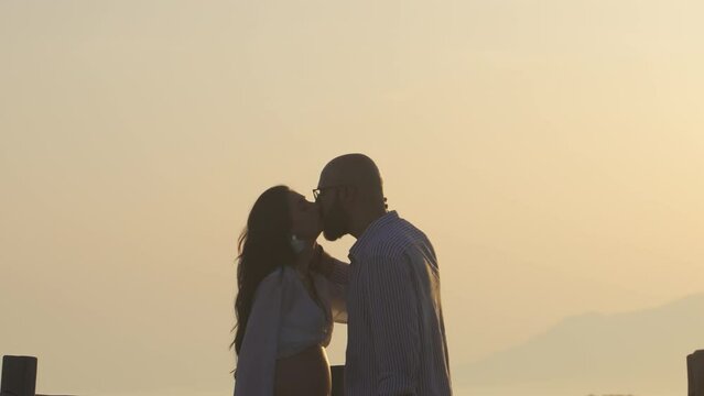 Silhouette of pregnant couple kissing during sundown