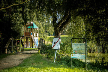Photographie d'une aire de jeux pr&egrave;s d'un &eacute;tang et de leurs signal&eacute;tiques. 
