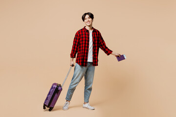 Traveler happy man wear red casual clothes hold bag passport boarding ticket isolated on plain beige background. Tourist travel abroad in free spare time rest getaway. Air flight trip journey concept.
