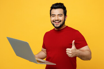 Satisfied side view smart young happy IT Indian man wearing red t-shirt casual clothes hold use...