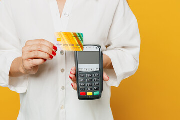 Cropped young happy woman she wears white shirt casual clothes hold wireless modern bank payment terminal to process acquire credit card isolated on plain yellow background studio. Lifestyle concept.