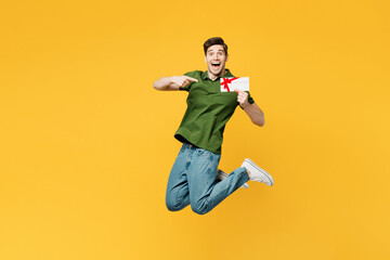 Fototapeta na wymiar Full body young happy man he wearing green t-shirt casual clothes jump high hold point finger on gift certificate coupon voucher card for store isolated on plain yellow background. Lifestyle concept.