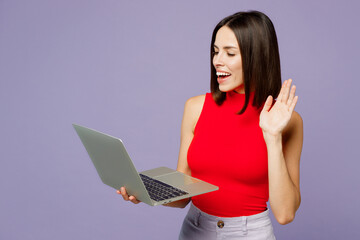 Fototapeta premium Young smiling happy cheerful IT woman she wears red tank shirt casual clothes hold use work on laptop pc computer waving hand isolated on plain pastel light purple background studio Lifestyle concept