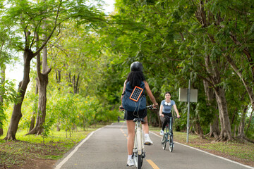 Rear view of Asian woman riding a bicycle in the park. It has a backpack with a solar panel for charging smartphone.
