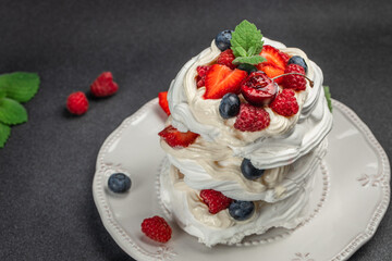 mini pavlova meringue cakes with whipped cream and fresh berries on a dark background, top view