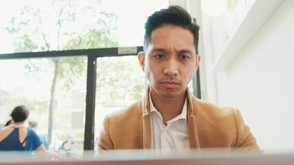 Close up, young handsome businessman wearing beige suit working with laptop in cafe