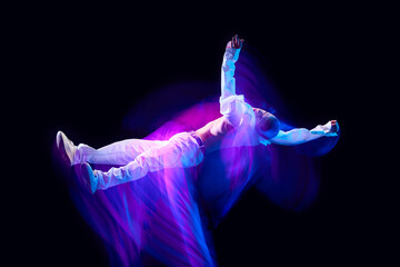 Freedom of movements. Young man in stylish clothes in motion against black studio background in neon with mixed lights effect. Concept of movements, art, dance and sport, fashion, youth, ad