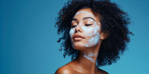 Cute girl with afro hair applying cream on face looking aside with blue background