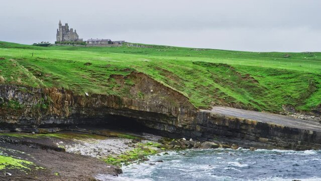 Ocean Waves Crashing Below Cliff and Classiebawn Castle In Distance