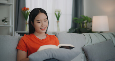 Asian woman reading a book while sitting on the sofa