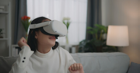 Asian woman watching a concert via VR glasses and dancing while sitting on the sofa