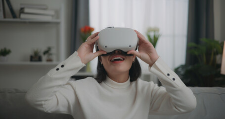 Asian woman watching a concert via VR glasses and dancing while sitting on the sofa