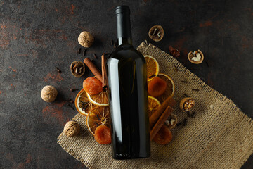 Glass bottle, dried fruits and nuts on dark background, top view