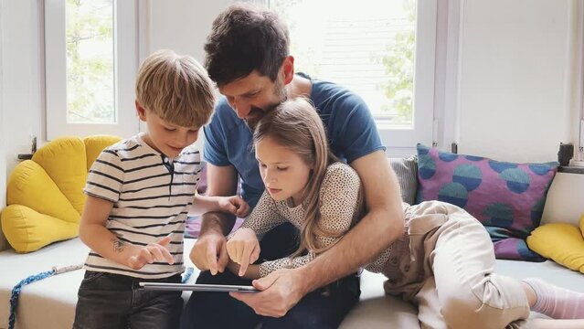 Father and children sitting on couch usig digital tablet