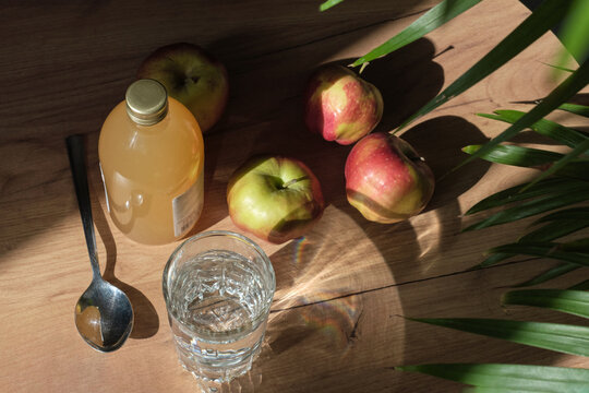 woman carefully pours apple cider vinegar into a spoon, adding it to a glass of water to create a healthy, invigorating drink. Drinking Apple Cider Vinegar: From Weight Loss to Improved Digestion