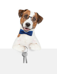 Smart Jack russell terrier puppy wearing tie bow and eyeglasses holds in his paw the keys to a new apartment over a blank banner. Isolated on white background