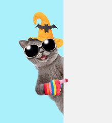 Happy cat wearing hat for halloween and sunglasses points away on empty white banner. isolated on blue background