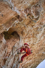 Strong male alpinist in safety equipment climbing on rocky cliff