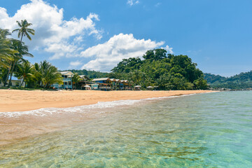 Deserted sandy beach on tioman island malaysia with crystal clear water palm trees and local houses.