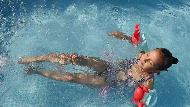 Happy girl in swimsuit and armbands enjoying a swim in the pool