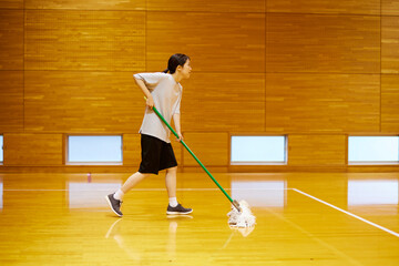 体育館にてモップで掃除をするスポーツウェアを着た日本人女性