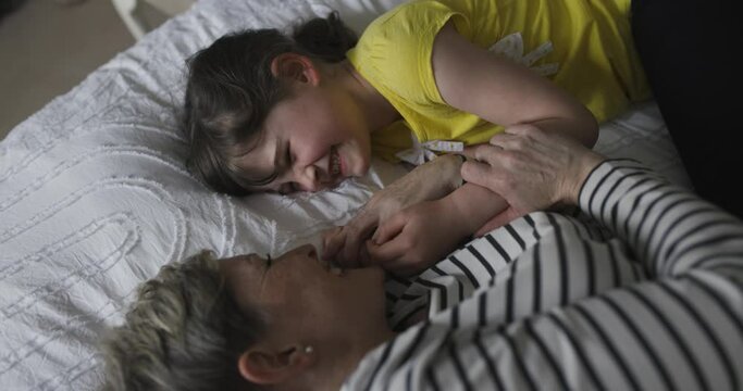 Mother and daughter smiling and holding hands on bed
