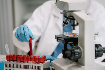 Doctor taking a blood sample tube from a rack with machines of analysis in the lab background, Technician holding blood tube test in the research laboratory.