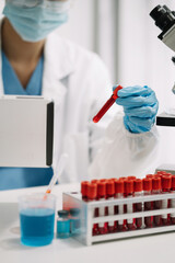 Doctor taking a blood sample tube from a rack with machines of analysis in the lab background,...