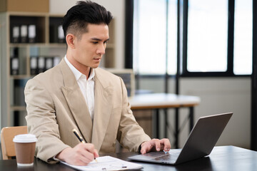 Male writes information businessman working on laptop computer writing business plan while sitting in office.