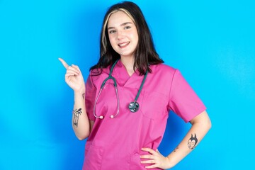 Young caucasian doctor woman wearing pink medical uniform looking at camera indicating finger empty space sales
