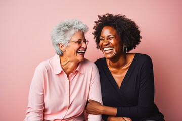 Portrait of two older female interracial best friends laughing, smiling and hugging on solid studio background.