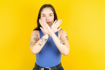 Beautiful woman wearing blue tank top has rejection expression crossing arms and palms doing...