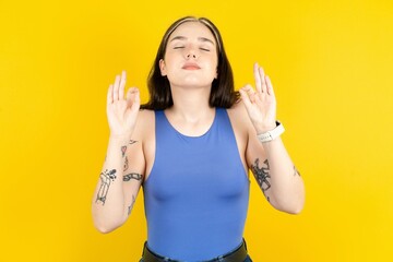 Beautiful woman wearing blue tank top relax and smiling with eyes closed doing meditation gesture with fingers. Yoga concept.